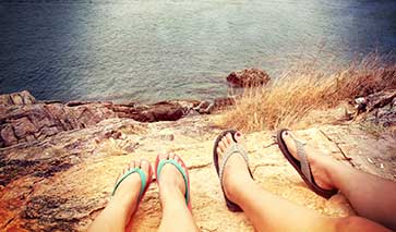 Two pairs of feet with sandals by the coast