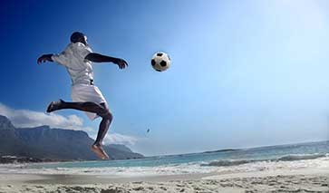 Footballer about to kick a football on the beach