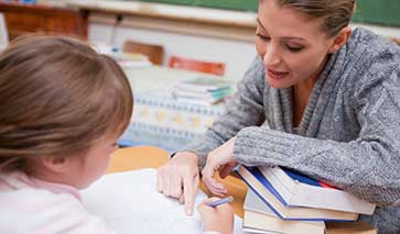 Primary school teacher teaching a young pupil