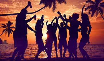 Partygoers at a beach party silhouetted by the setting sun