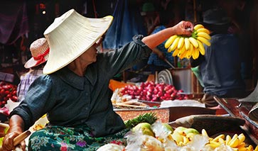 Thailand market place on a river, seller clutching a bunch of bananas