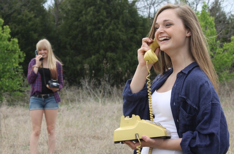 Two girls on phones in a field 