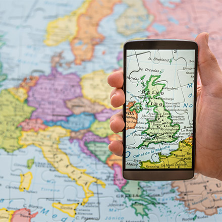 Hand holidng phone with a map of UK over a map of Europe