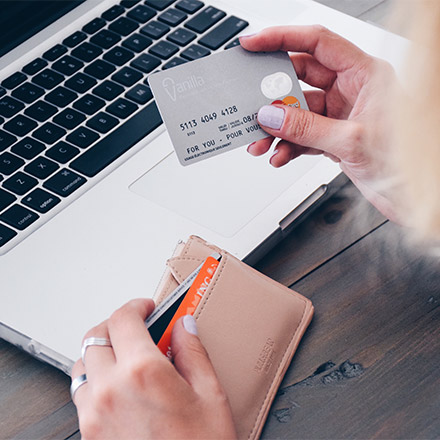 Woman holding bank care in front of laptop