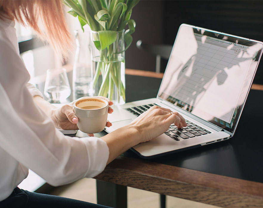 Woman using laptop with coffee in hand