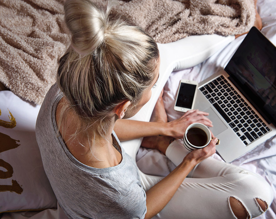 Girl using laptop on bed with a cup of coffee