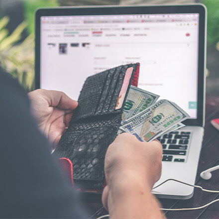 Man holding wallet with money in front of laptop