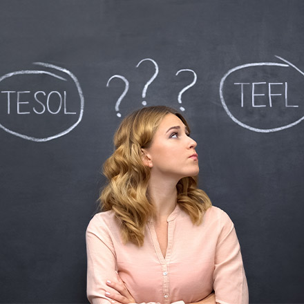 Woman stood in front of chalk board with TEFL and TESOL wrote on it