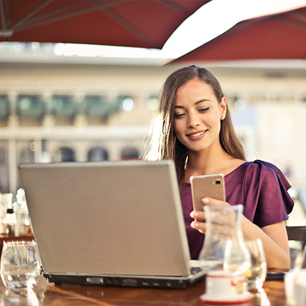 Woman using phone and laptop at outdoor cafe