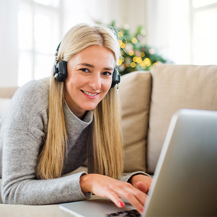 Woman laid on sofa with headphone using laptop