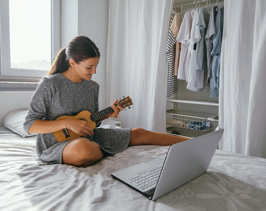 Woman sat on bed learning ukulele