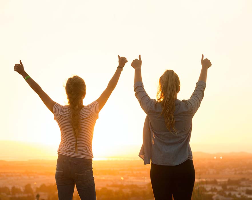 two TEFL teachers looking into the sunset with their thumbs up