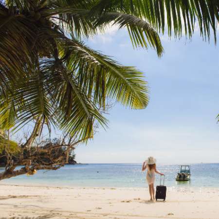 Woman on beach in Thailand with her suitcase