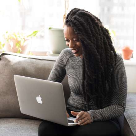 WOMAN SMILING AT LAPTOP ON SOFA